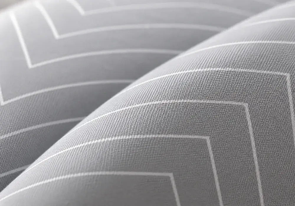 Macro sul tessuto grigio a sottili spighe bianche del cuscino, luce radente che rivela la trama